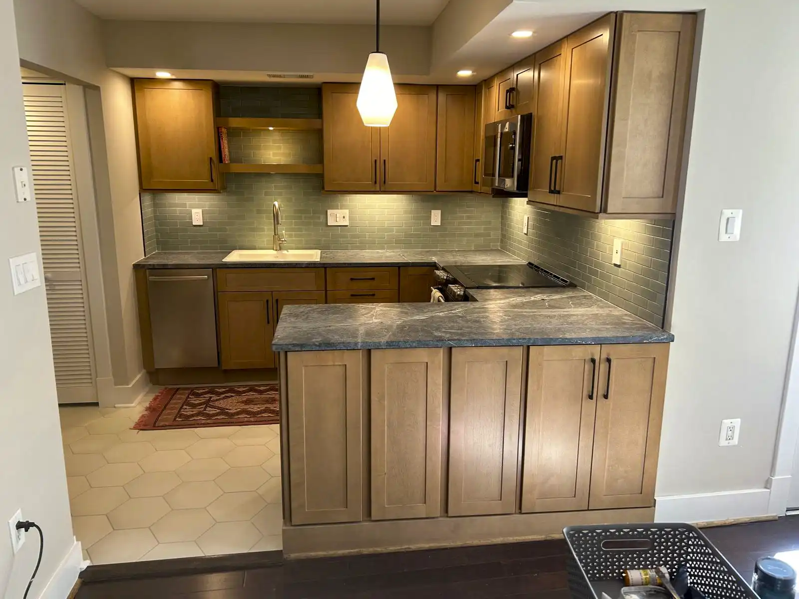Kitchen with wood-finish cabinets, a stone-look countertop, tiled backsplash and peninsula.