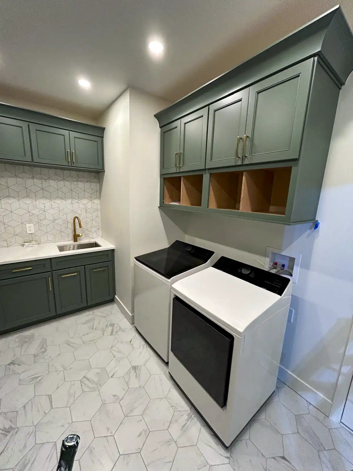 Laundry room with green cabinets, a sink, washer, dryer and hexagonal floor tiles.